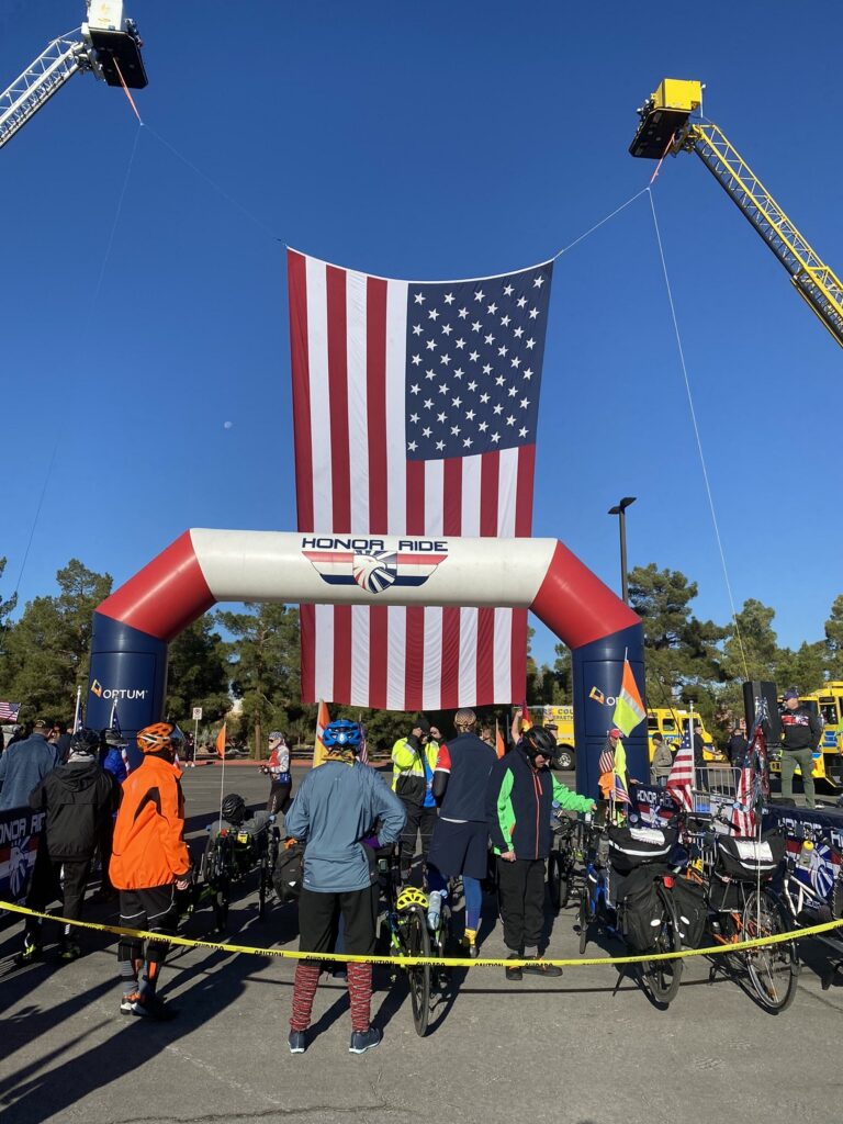Crowd ready to take off under starting arch and flag at Honor Ride